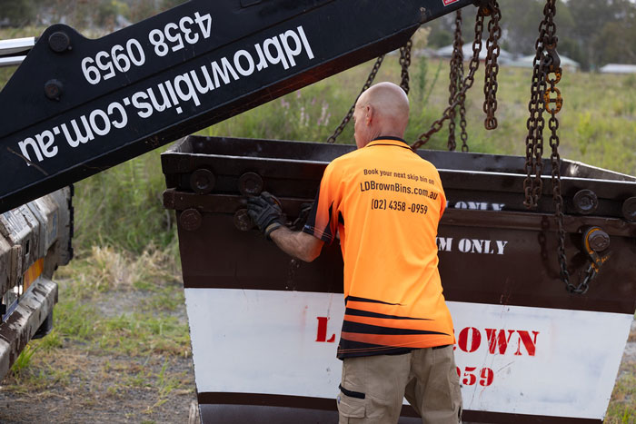 Worker operating a towing crane near a dumpster.